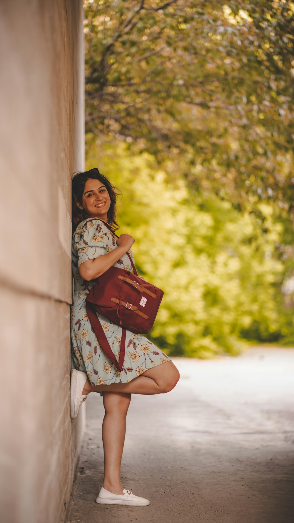 a woman leaning against a wall holding a red purse