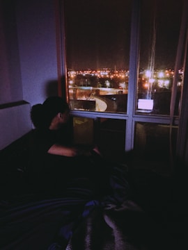 A shadowy figure observing a busy city street from a darkened room.