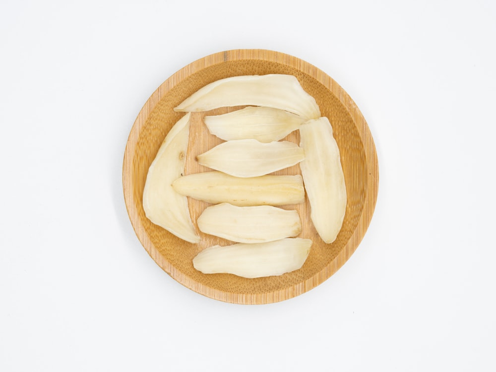 a wooden bowl filled with peeled bananas on top of a white table