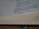 Open book with printed text visible on the right side of the page. The text appears to be from a religious or philosophical context, and the book is set on a wooden surface with a green ribbon bookmark.