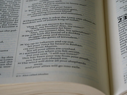 A glowing open Bible resting on a dark wooden table, bathed in soft candlelight.