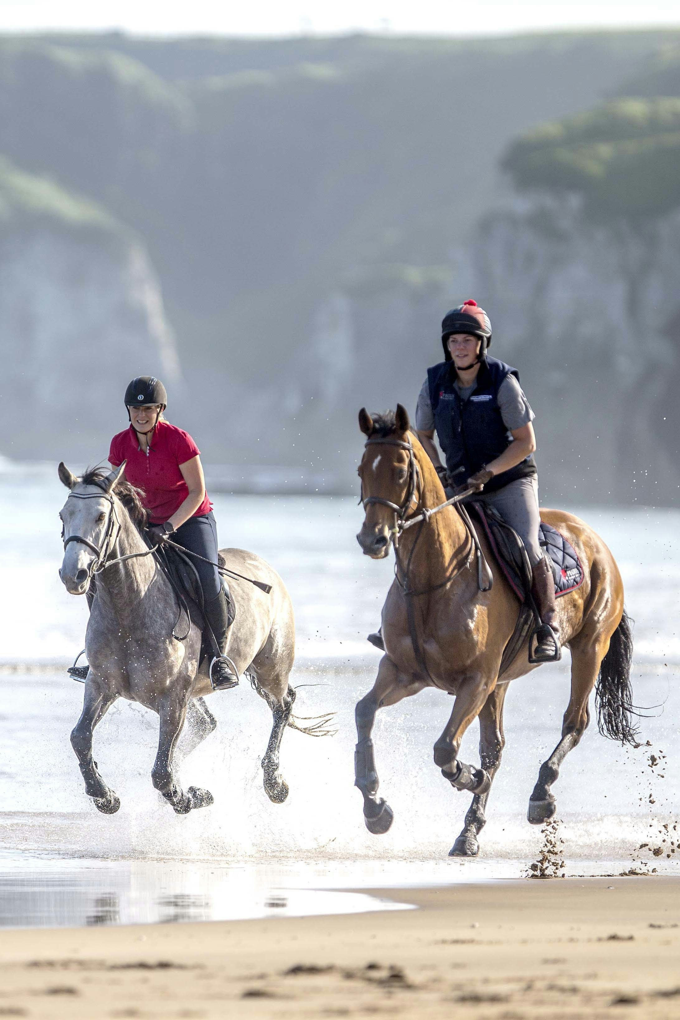 two people are riding horses on the beach