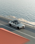 A stylish sedan cruising along a coastal road at sunset.