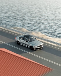 A sleek teal sedan driving along a coastal road during sunset.