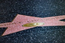 A star embedded in a black speckled pavement featuring the name 'Carole Lombard'. The star is pink with a brass emblem in the center, likely from the Hollywood Walk of Fame.