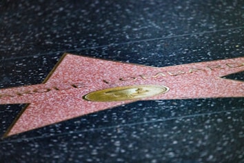 A star embedded in a black speckled pavement featuring the name 'Carole Lombard'. The star is pink with a brass emblem in the center, likely from the Hollywood Walk of Fame.
