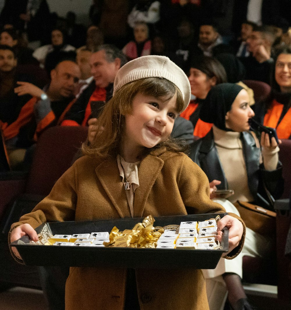 a young girl holding a tray of food in front of a crowd