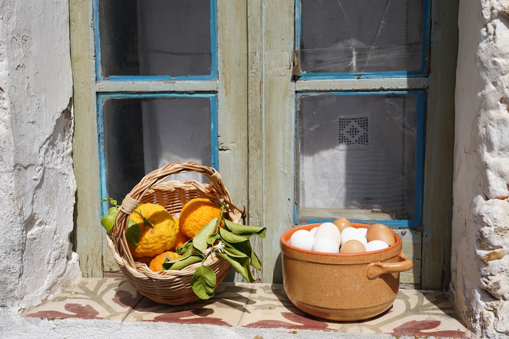 a basket of eggs sitting next to a bowl of fruit