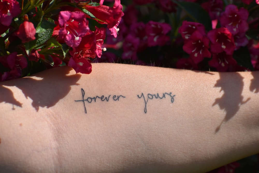 a close up of a person's arm with flowers in the background