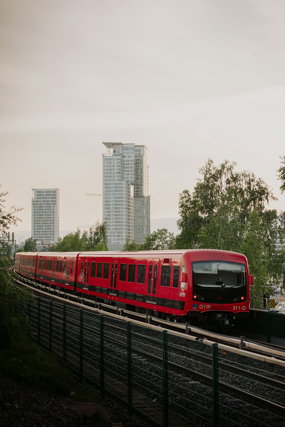 a red train traveling down train tracks next to tall buildings