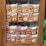 Packets of instant noodles are neatly arranged in a wooden display cabinet. The packaging features the brand 'Indomie Mi Goreng' with an image of cooked noodles topped with a fried egg. The display is organized in two rows, making the products clearly visible through the glass.