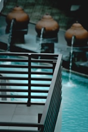 The image contains a decorative outdoor water feature with several spherical terracotta pots, each streaming water into a pool. The water is a striking turquoise, contrasting with the dark metal railing in the foreground.