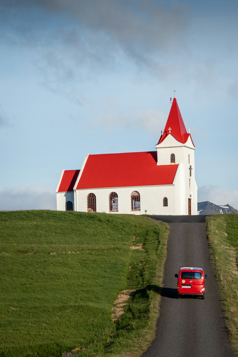 a red car driving down a road next to a white church
