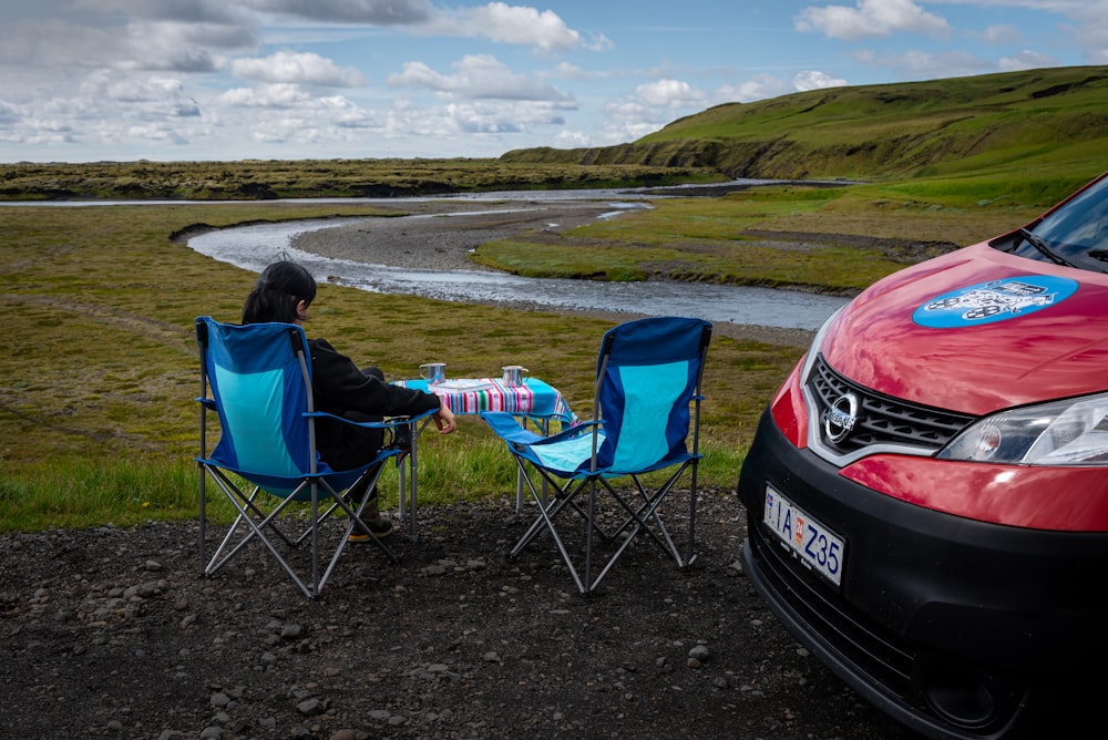 a person sitting in a chair next to a red car