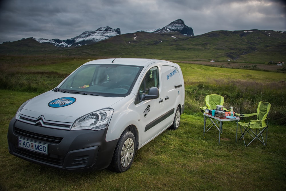 a small white van parked in a field next to a table and chairs