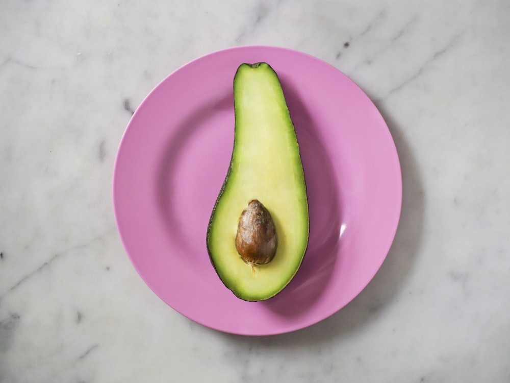 an avocado cut in half on a pink plate