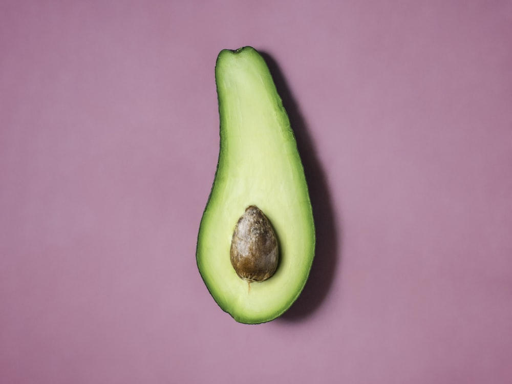 an avocado cut in half on a purple surface