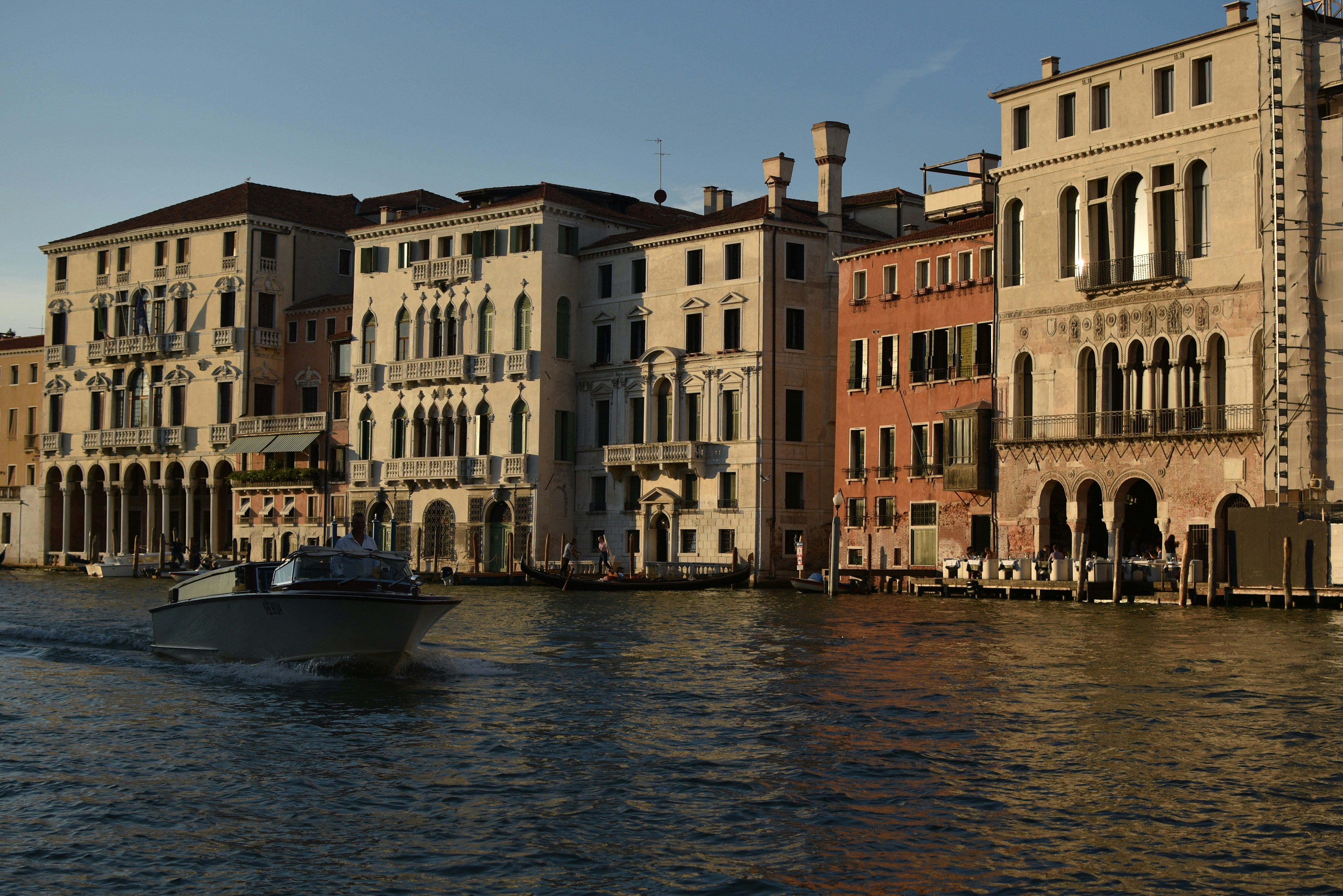 a boat traveling down a river next to tall buildings, Venice at dusk