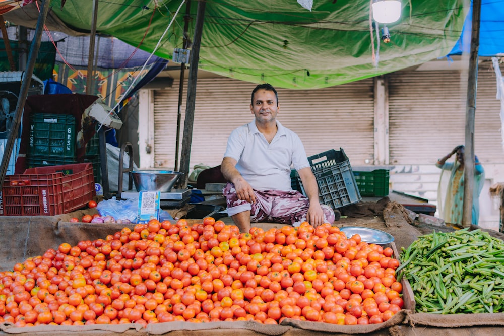 a man sitting in front of a large pile of fruit