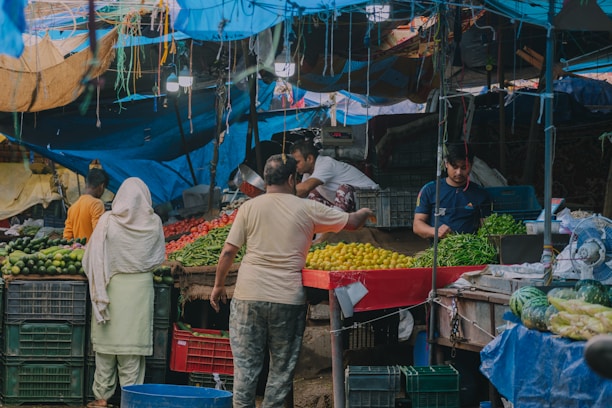Indian farmers in a village collection centre, sorting crates of vegetables and fruits with scales and carts ready for market transport.