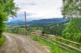A scenic view of rural land with a dirt road and a wooden fence.