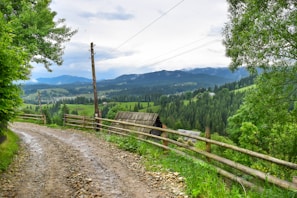 A scenic view of rural land with a dirt road and a wooden fence.