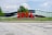 Large red letters spelling out 'EPFL' stand in front of a modern, curved glass building. The surrounding area features green grass and a few trees. The sky is partly cloudy, creating a bright and open atmosphere.