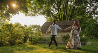 A couple holding hands and walking through a lush garden filled with colorful blossoms and greenery.