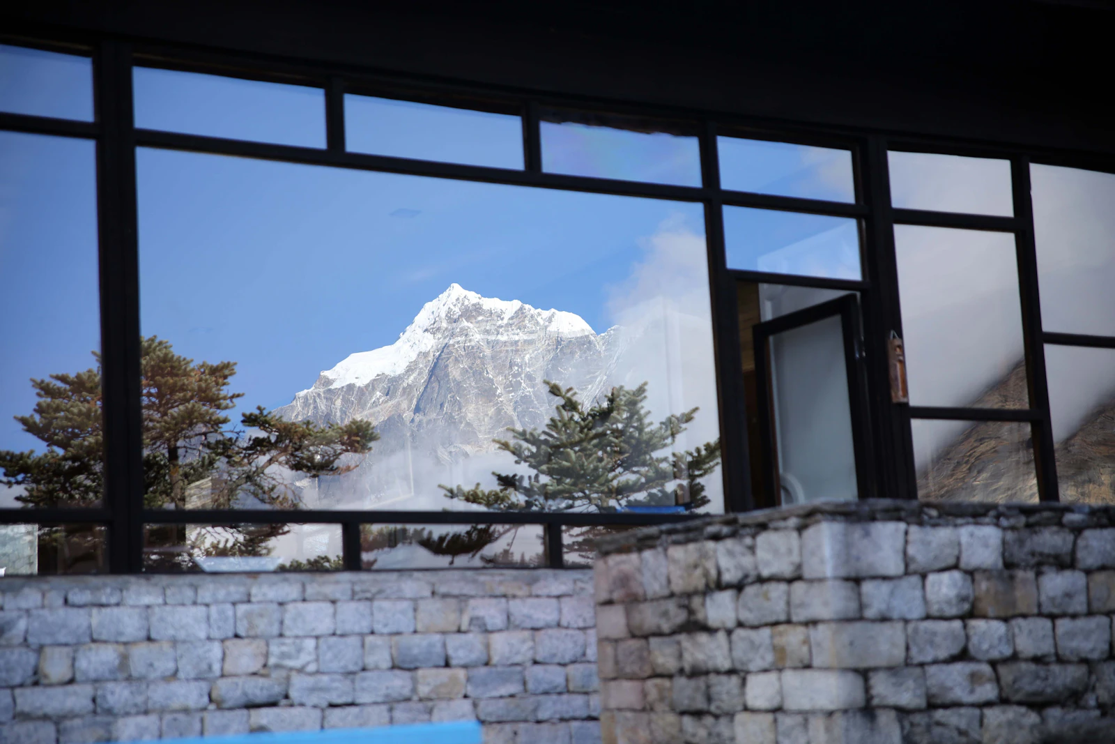 A snow peak seen through the tall windows of Hotel Everest View above its dry-stone wall, in the Everest region of Nepal