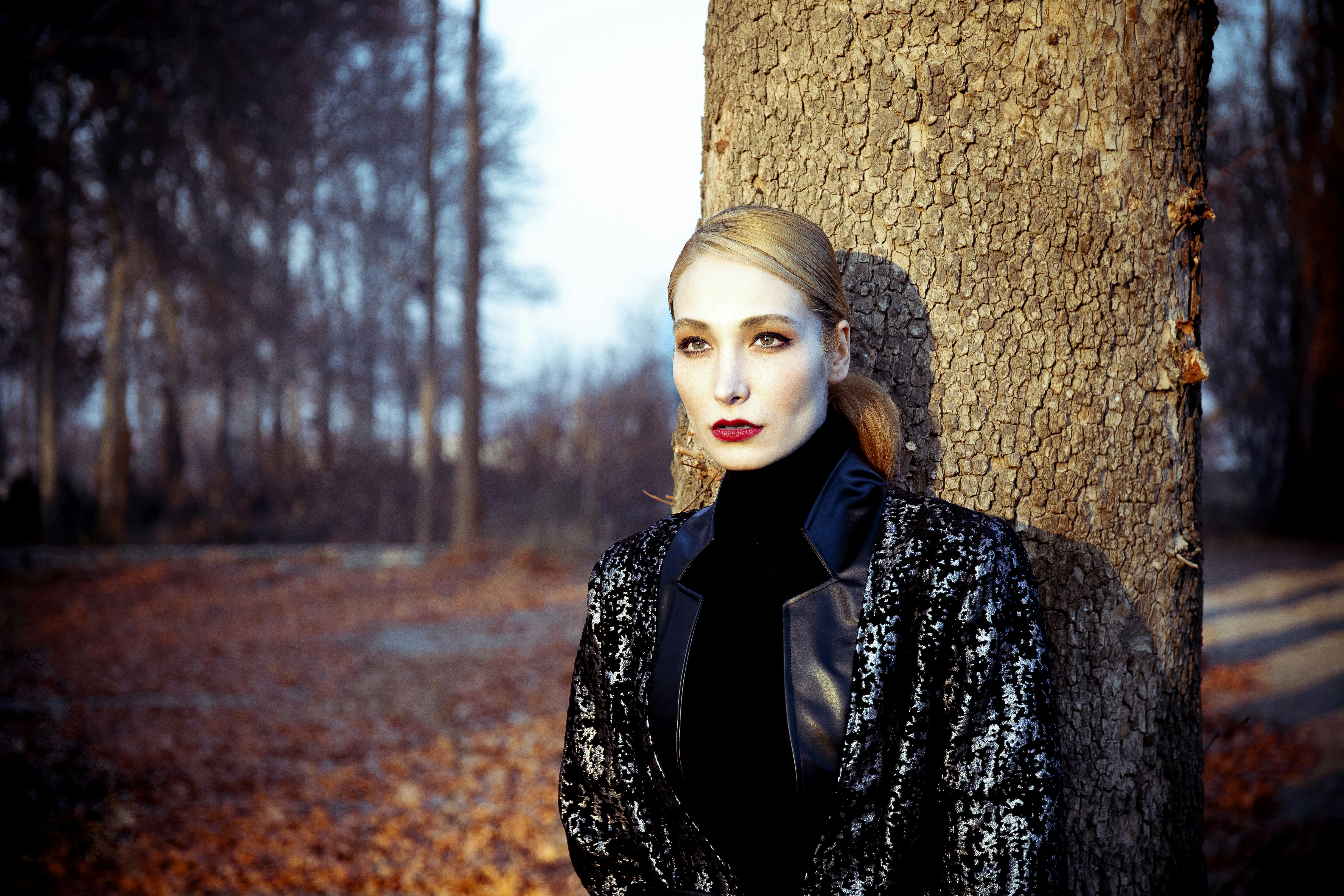 a woman standing next to a tree in a forest