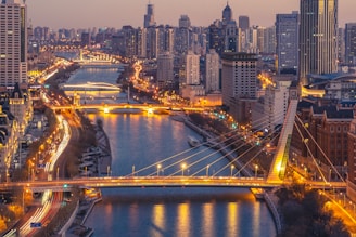 A sleek aerial view of a bustling metropolitan area at dusk, highlighting illuminated bridges and highways.