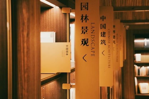 A series of bookshelves lined with books are labeled with vertical signs. The focus is on a sign with the words 'LANDSCAPE' in English and Chinese characters. The lighting is warm, creating a cozy atmosphere in the wooden interior.