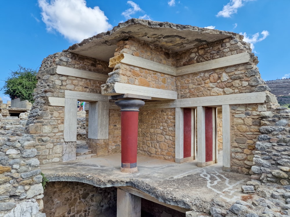 un edificio in pietra con una colonna rossa di fronte ad esso