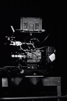 A professional video camera setup with a mounted camera and various attached components, including cables and a monitor. The setup is positioned against a dark background, highlighting the intricate details and controls of the equipment.