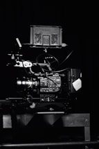 A professional video camera setup with a mounted camera and various attached components, including cables and a monitor. The setup is positioned against a dark background, highlighting the intricate details and controls of the equipment.