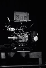 A professional video camera setup with a mounted camera and various attached components, including cables and a monitor. The setup is positioned against a dark background, highlighting the intricate details and controls of the equipment.