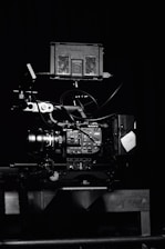 A professional video camera setup with a mounted camera and various attached components, including cables and a monitor. The setup is positioned against a dark background, highlighting the intricate details and controls of the equipment.