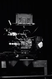 A professional video camera setup with a mounted camera and various attached components, including cables and a monitor. The setup is positioned against a dark background, highlighting the intricate details and controls of the equipment.