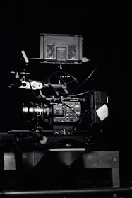 A professional video camera setup with a mounted camera and various attached components, including cables and a monitor. The setup is positioned against a dark background, highlighting the intricate details and controls of the equipment.
