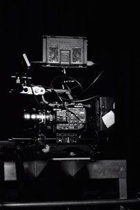A professional video camera setup with a mounted camera and various attached components, including cables and a monitor. The setup is positioned against a dark background, highlighting the intricate details and controls of the equipment.