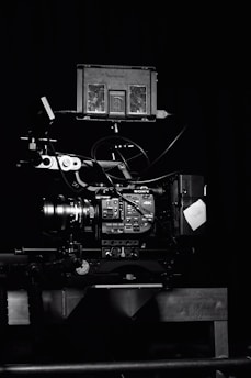 A professional video camera setup with a mounted camera and various attached components, including cables and a monitor. The setup is positioned against a dark background, highlighting the intricate details and controls of the equipment.