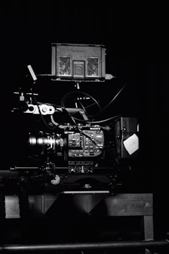 A professional video camera setup with a mounted camera and various attached components, including cables and a monitor. The setup is positioned against a dark background, highlighting the intricate details and controls of the equipment.