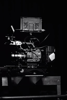 A professional video camera setup with a mounted camera and various attached components, including cables and a monitor. The setup is positioned against a dark background, highlighting the intricate details and controls of the equipment.
