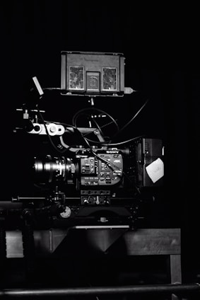 A professional video camera setup with a mounted camera and various attached components, including cables and a monitor. The setup is positioned against a dark background, highlighting the intricate details and controls of the equipment.