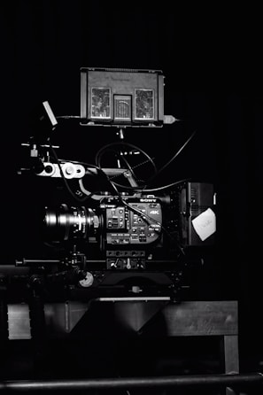 A professional video camera setup with a mounted camera and various attached components, including cables and a monitor. The setup is positioned against a dark background, highlighting the intricate details and controls of the equipment.