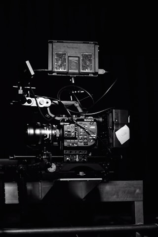 A professional video camera setup with a mounted camera and various attached components, including cables and a monitor. The setup is positioned against a dark background, highlighting the intricate details and controls of the equipment.