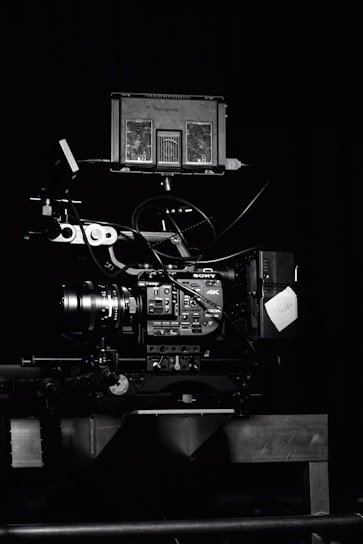 A professional video camera setup with a mounted camera and various attached components, including cables and a monitor. The setup is positioned against a dark background, highlighting the intricate details and controls of the equipment.