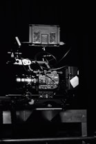 A professional video camera setup with a mounted camera and various attached components, including cables and a monitor. The setup is positioned against a dark background, highlighting the intricate details and controls of the equipment.