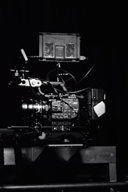 A professional video camera setup with a mounted camera and various attached components, including cables and a monitor. The setup is positioned against a dark background, highlighting the intricate details and controls of the equipment.