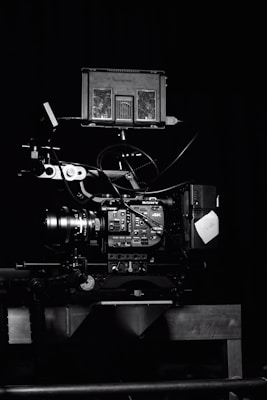A professional video camera setup with a mounted camera and various attached components, including cables and a monitor. The setup is positioned against a dark background, highlighting the intricate details and controls of the equipment.